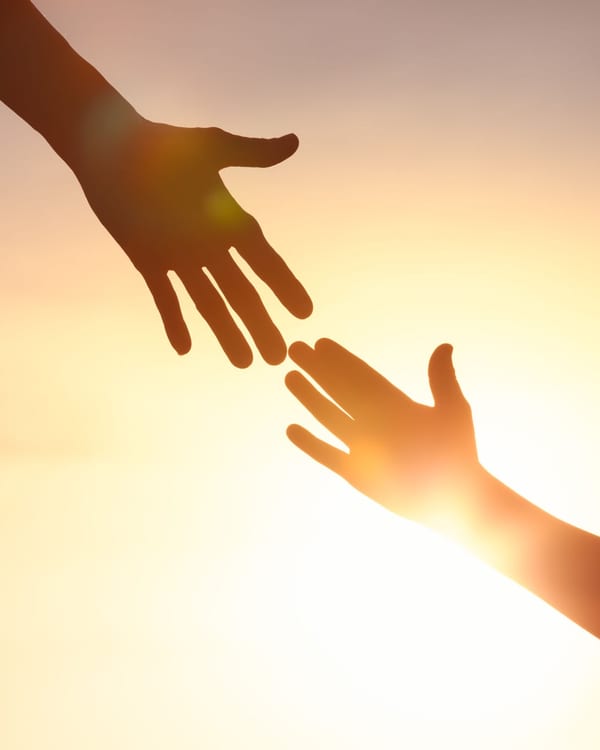 Two hands reaching toward each other at sunset, symbolising support and connection